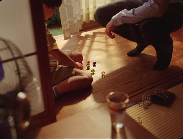 Boy playing with marbles and an adult man sitting in front of him interacting