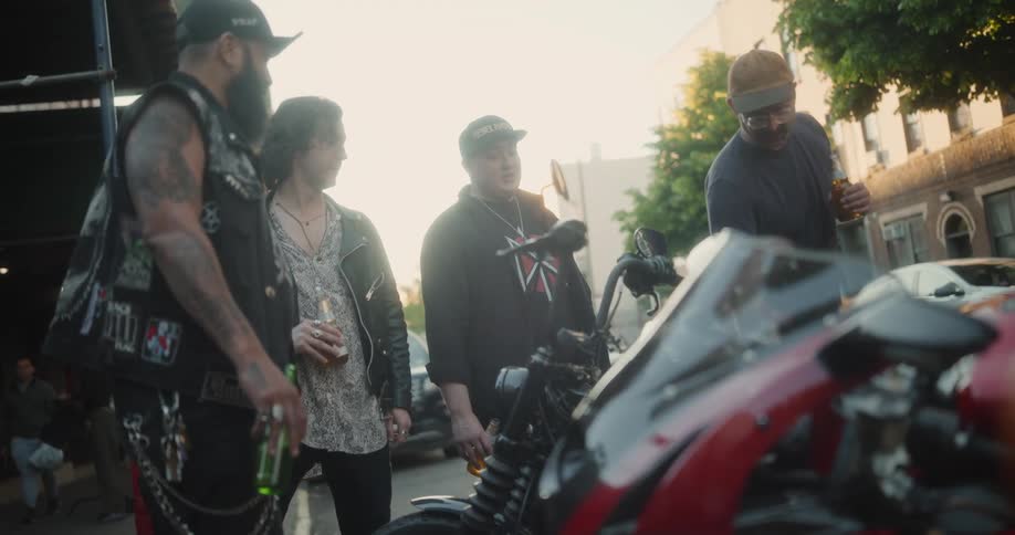 Bikers chat and enjoy beers around their motorcycles on a city street