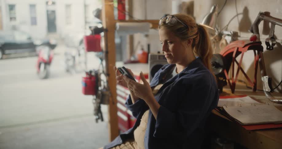 Woman sitting in a mechanics workshop using a smartphone