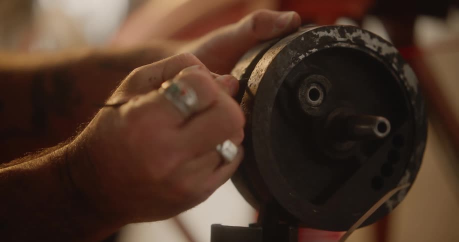 Man with a tattoo cleans part of a machine while in the workshop