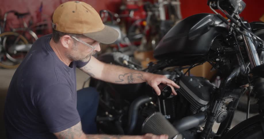 A mechanic working on a black motorcycle in a workshop adjusting or fixing a part of the motorcycle