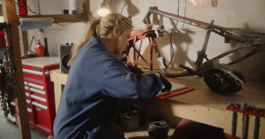 A mechanic studies a users manual while leaning over a workbench in the workshop