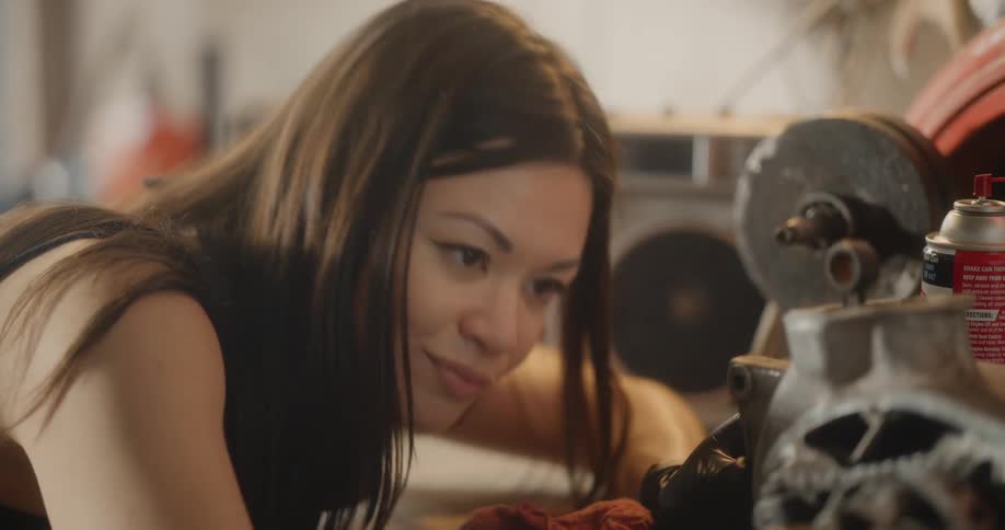 A young hispanic female spins a gear on a car part in a garage