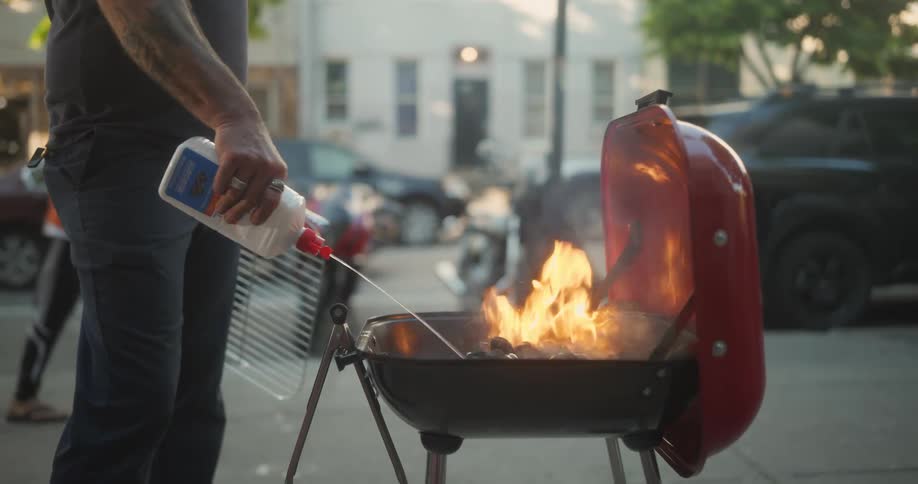 A man pours lighter fluid on the charcoal in an outdoor grill