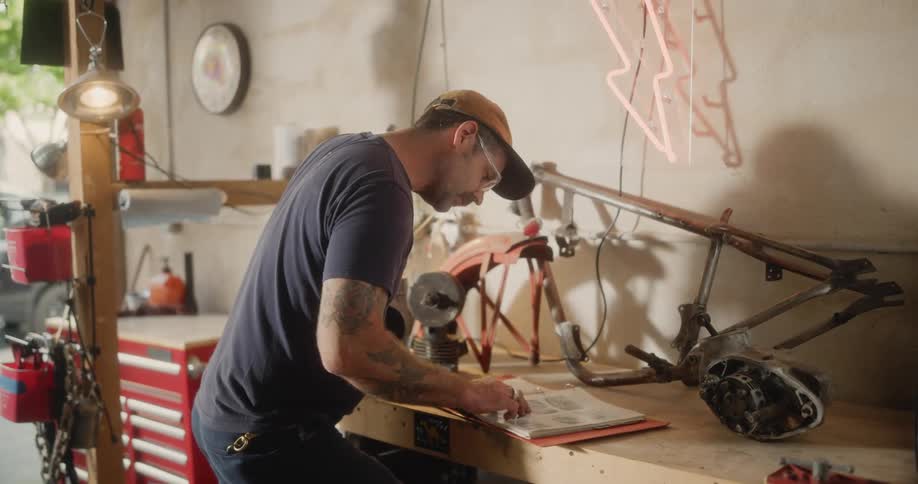 A mechanic studies a users manual while leaning over a workbench in the workshop