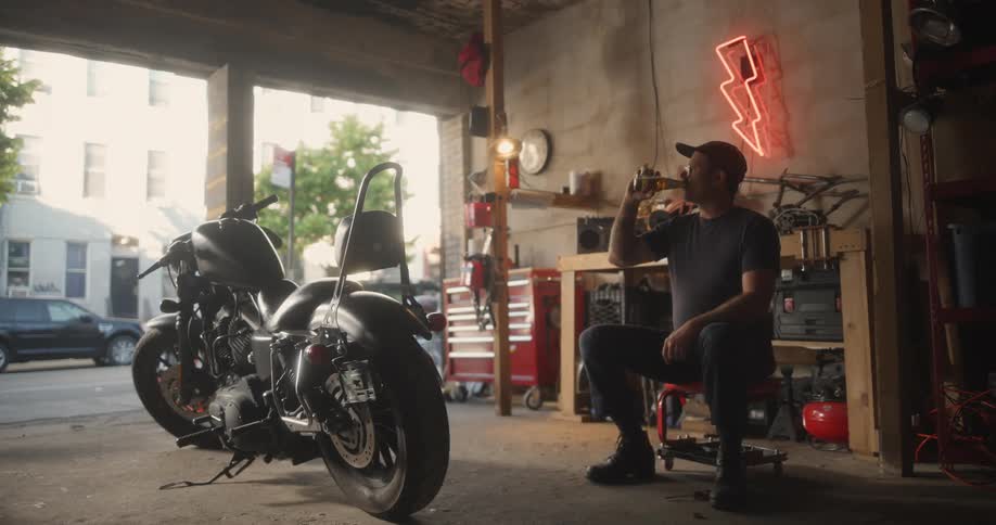Man sits in a garage near the street and drinks a bottled beverage