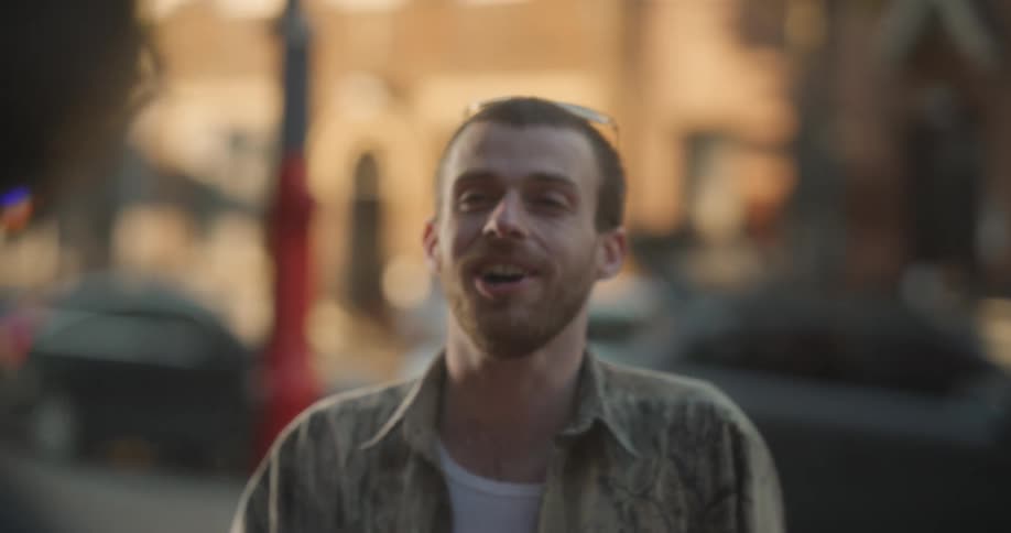 A man is casually smoking a cigarette outdoors while talking and laughing with a friend