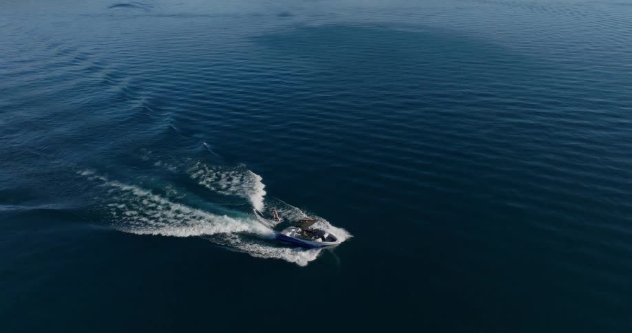 A boat glides across a vast expanse of water leaving a vshaped wake behind it with a person wakeboarding behind it