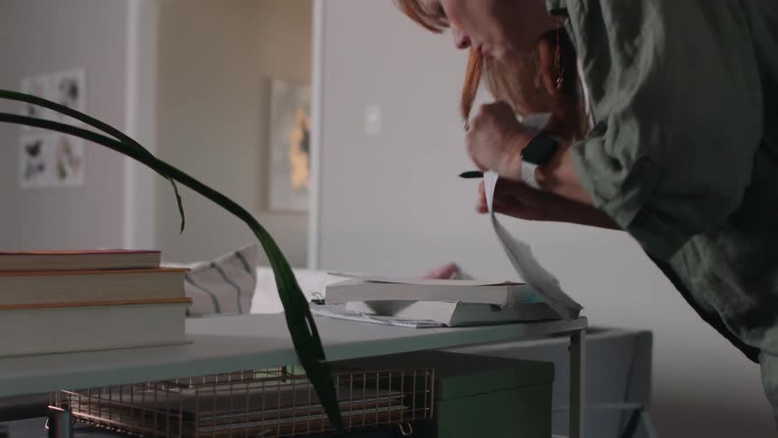 A woman is writing something on paper using a black pen