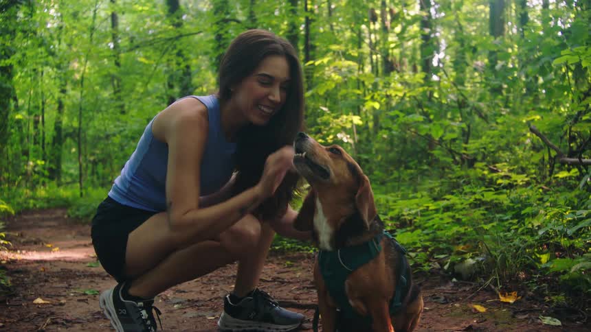 Happy woman petting her dog while they are on a trail through the forest