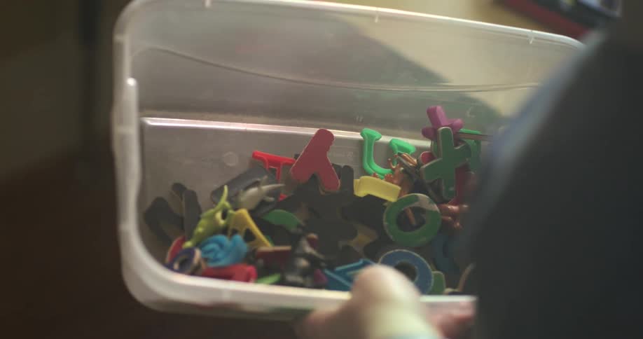 A woman carries a plastic container holding various toys inside a house