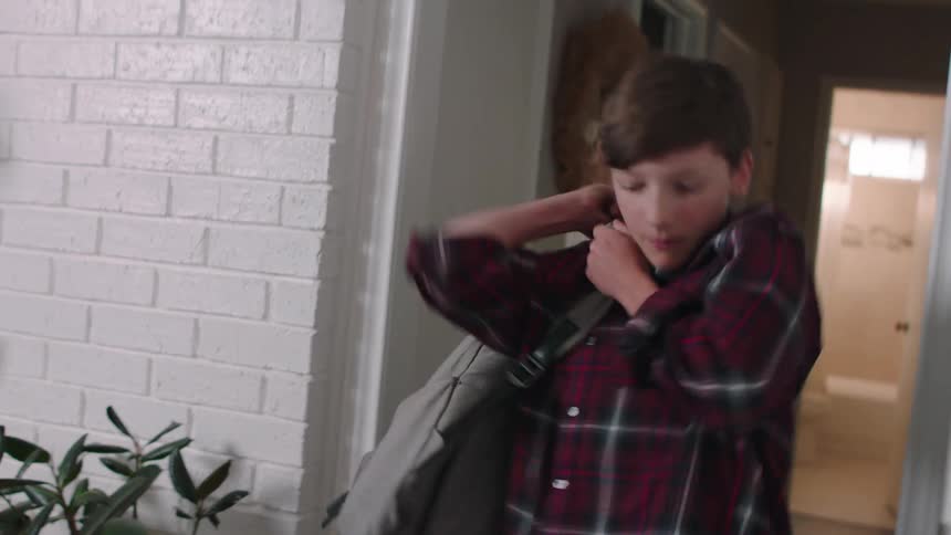 Boy picking up a backpack that is on the floor putting it on his back and leaving the house