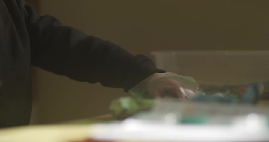 A hand of a person wearing a longsleeved black shirt and his hand is inside a plastic bag picking something up