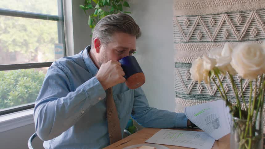 Man having a drink from a cup while reading some documents at a table