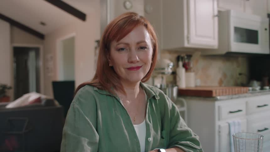 Woman sitting at the table in the kitchen giving a smile