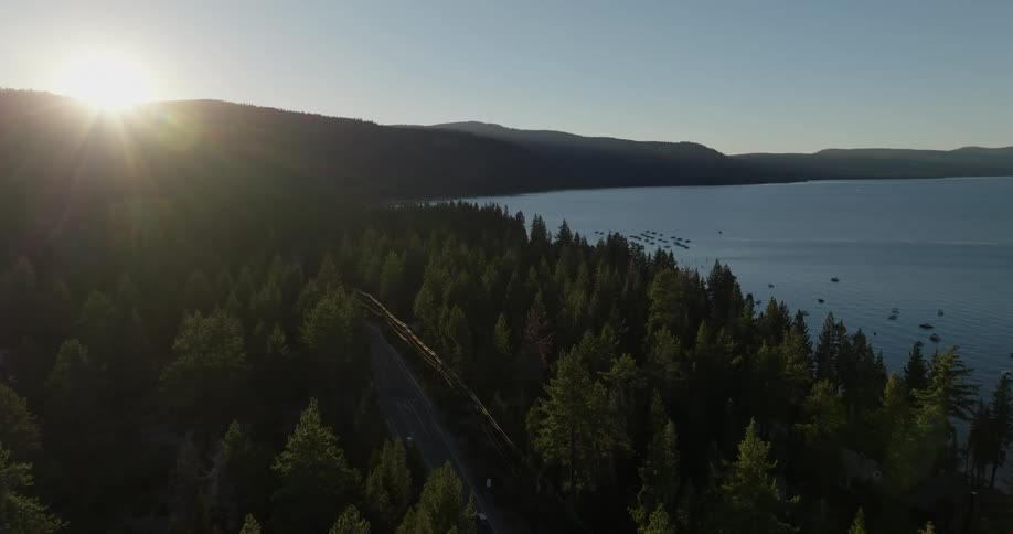 Aerial view of a highway surrounded by conifers on the edge of a lake and with sound on the horizon amid the silhouette of mountains