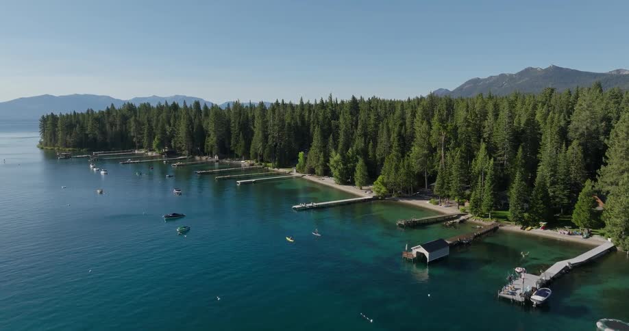 A serene lake surrounded by dense trees and dotted with boats under a clear blue sky