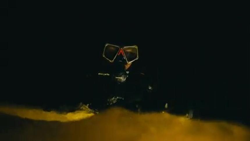 A person putting on a mask and diving equipment and diving underwater in a completely dark environment