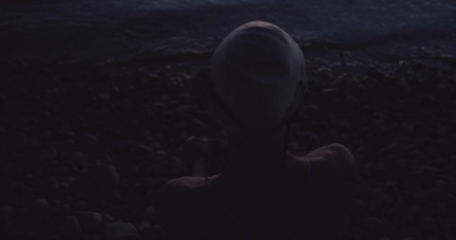View of a woman from behind with a white swimming cap getting ready in front of a lake on a dark dawn
