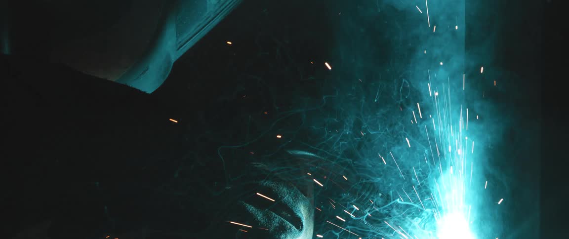 Person with protective helmet welding an object and emitting sparks and smoke