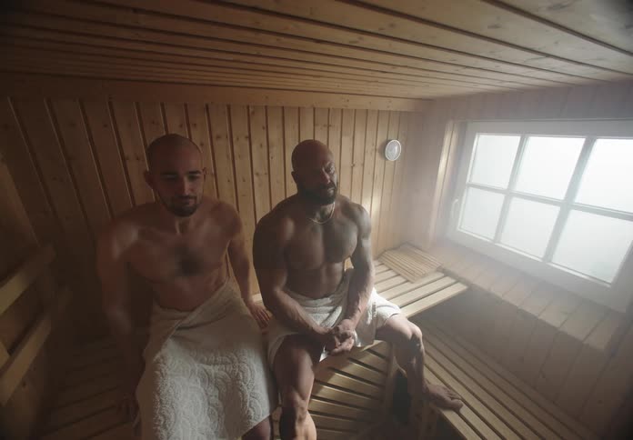 Two men in a sauna with one of them moving away from the other