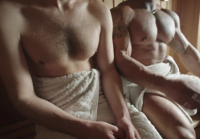 A wellbuilt man takes a seat next to another person in a sauna