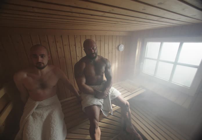 Man walking away from another man after exchanging glances while both are in towels sitting in a sauna