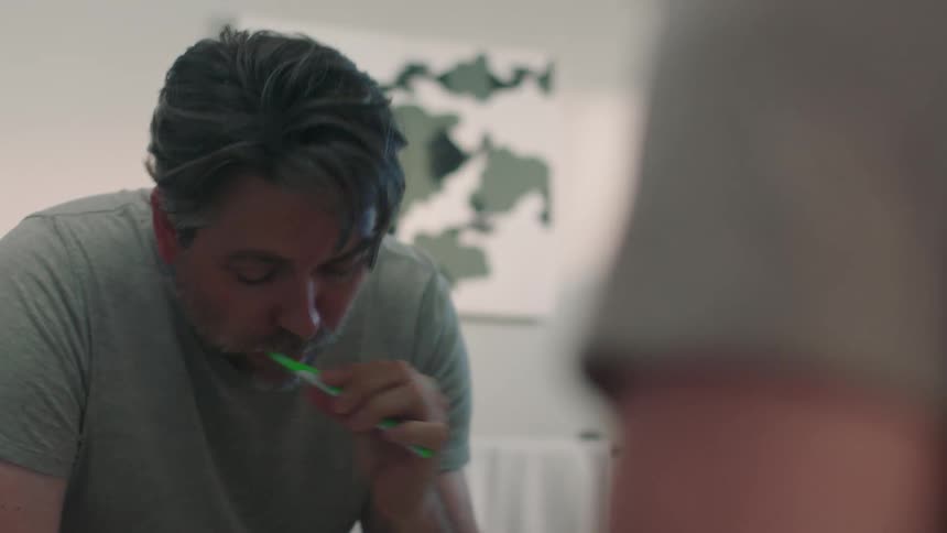 A man reflected in a bathroom mirror while washing his teeth