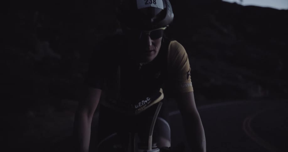 A cyclist in motion wearing a helmet and sunglasses either at dawn or dusk