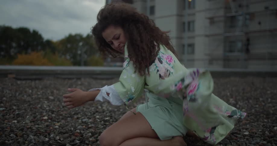 Woman with angry expression is kneeling on the rocks and getting up