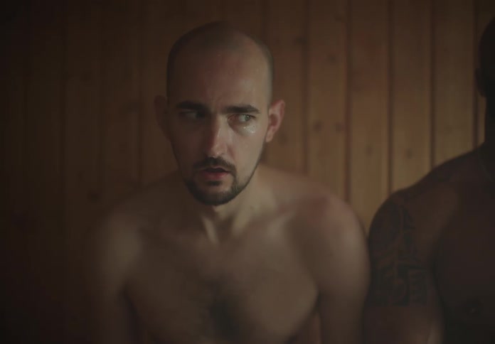 Man sitting in a sauna side eyes the larger man sitting next to him
