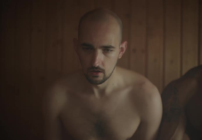 Inside a sauna a man sits nervously glancing at the person uncomfortably close to him