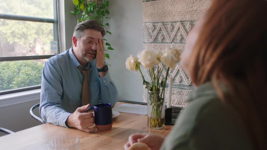 Man in tie sitting at table with a cup talking to his wife