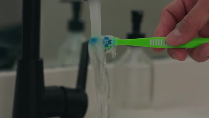 Close up of a hand holding a toothbrush being washed in the sink