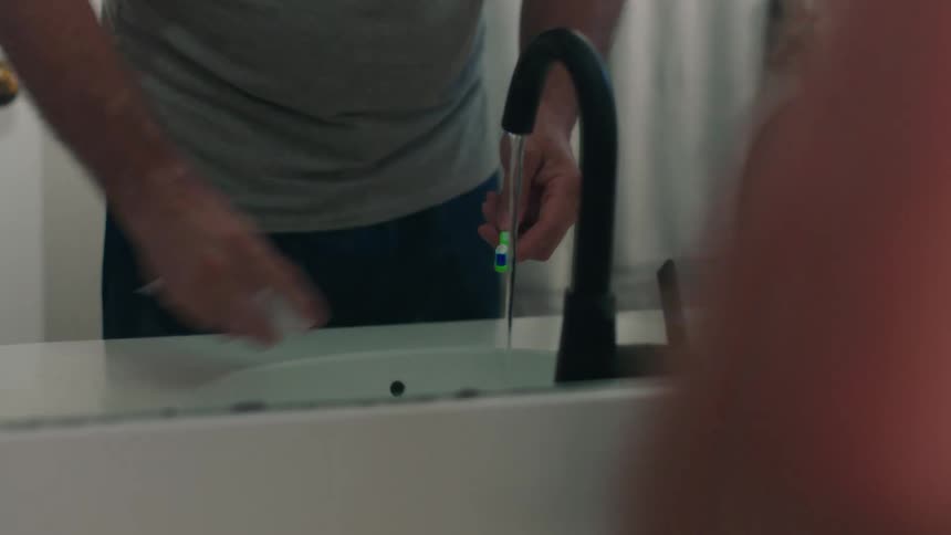 A man applies tooth paste to a green toothbrush brushing his teeth
