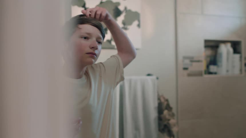 A boy fixes his hair in the mirror