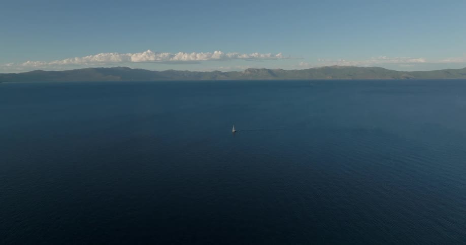Aerial view of a sailboat in a vast ocean under a clear sky