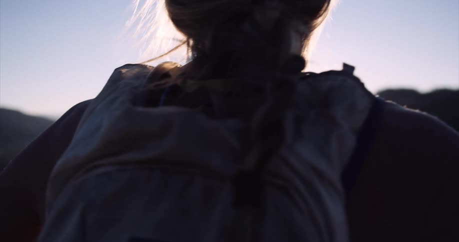 View of a woman from behind on a mountain peak enjoying the natural landscape with the sun on the horizon