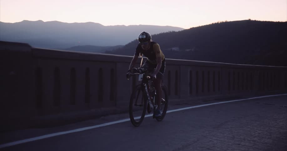 Cyclist pedaling uphill on a paved road with the silhouette of mountains on the horizon at sun rise