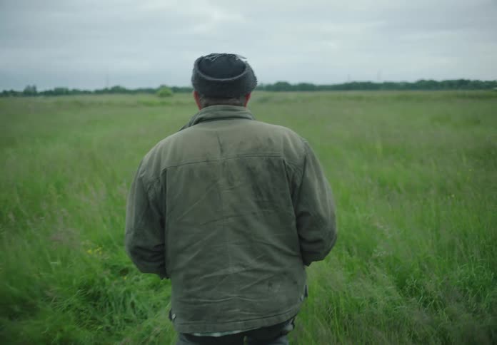 A man walks in a field of tall grass seen from behind