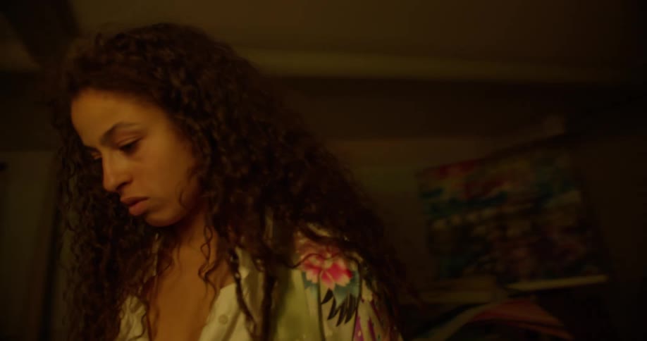 Portrait of a curly haired woman in a low lit room picking up a painting