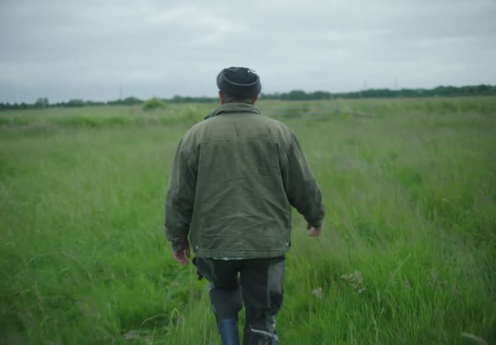A man in a coat walks across a large grassy plain