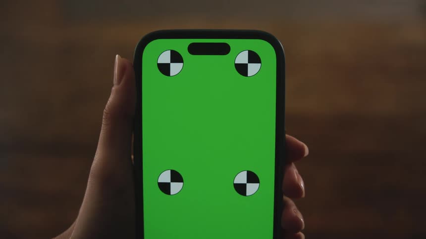 A woman holds up a cell phone with a green screen with black and white circles on it