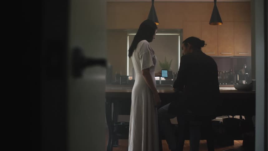 Woman stands and shows smartphone screen to man sitting nearby in their home