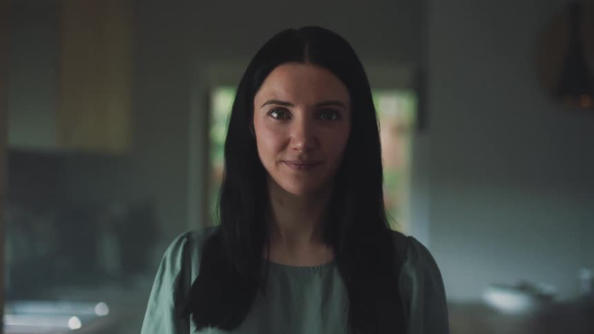 A woman is standing in the kitchen smiling as she looks ahead