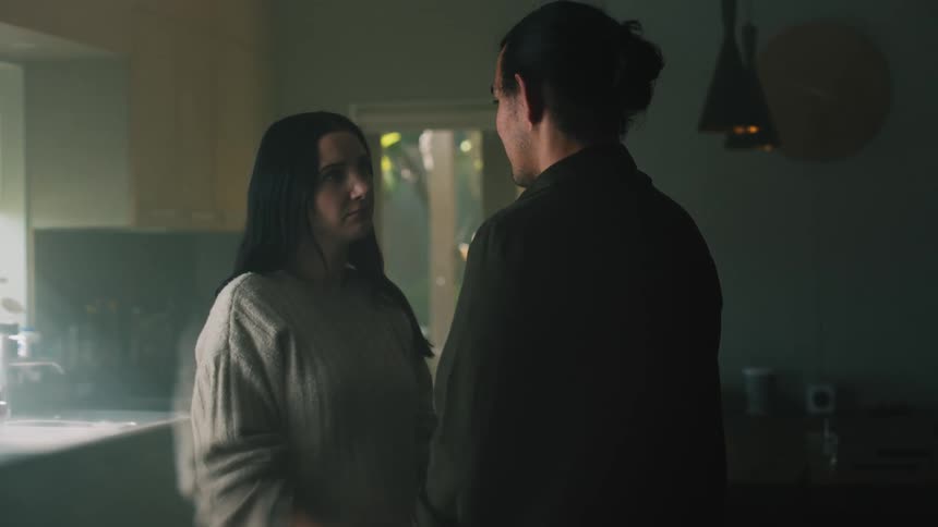 A woman is standing in a kitchen speaking to a man