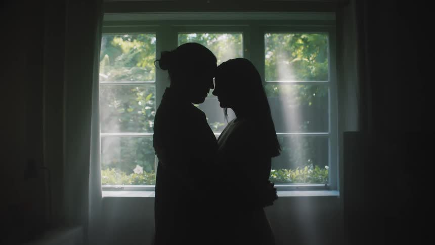 Man and woman holding each other are silhouetted against the window