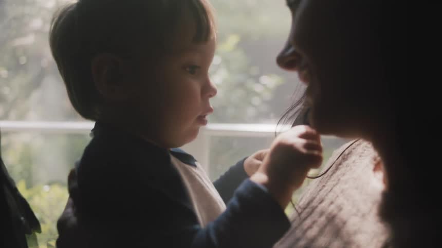 Close up of a toddler playing with his mother hair near a window at home in the morning
