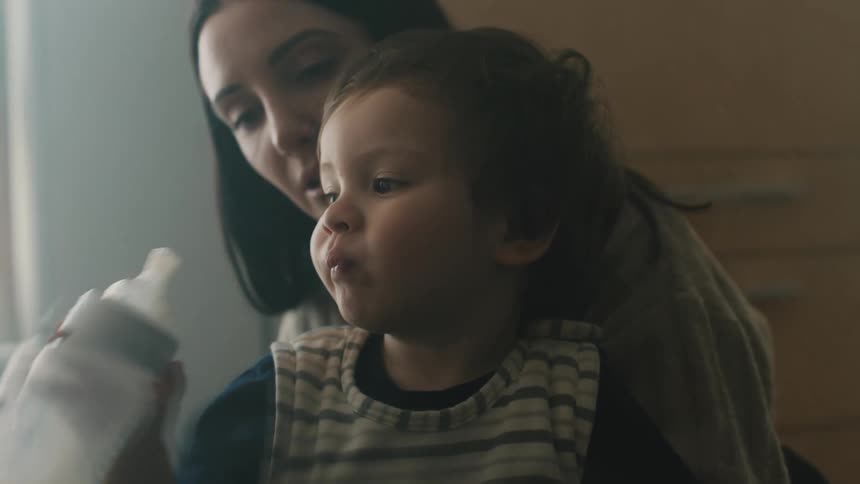 Mother holds son while he drinks from a bottle