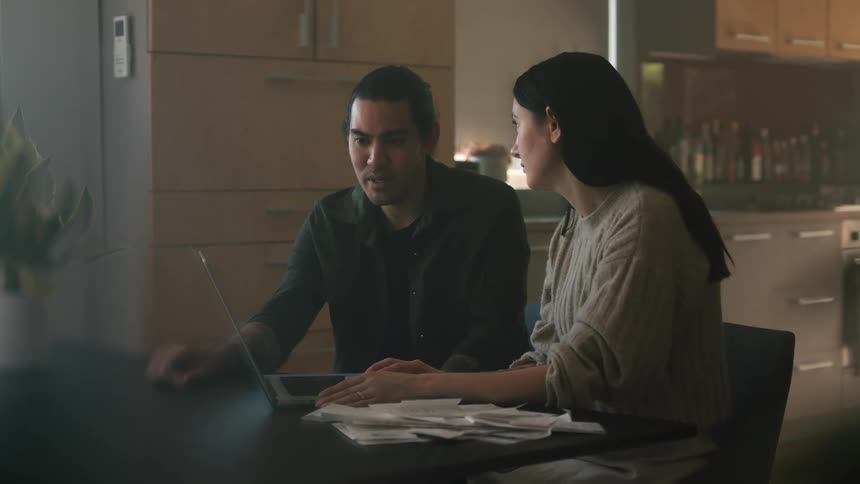 Man with black jacket and woman with black straight hair and gray sweater use laptop in the kitchen